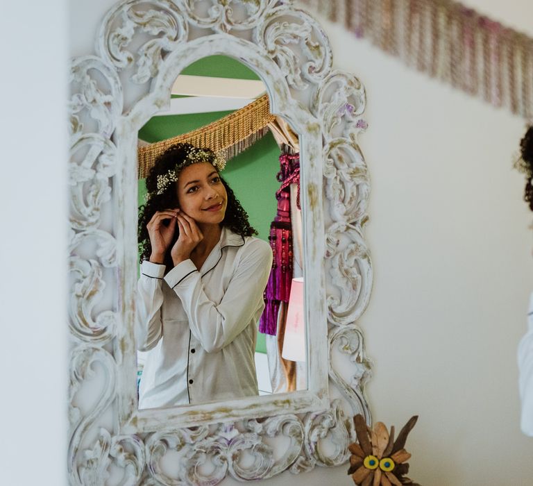 Bride applies her earrings whilst looking in the mirror on her wedding day 