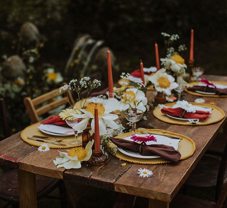 Intimate sixties wedding reception table decor with white peonies, orange candles, brown vases and yellow placemats 