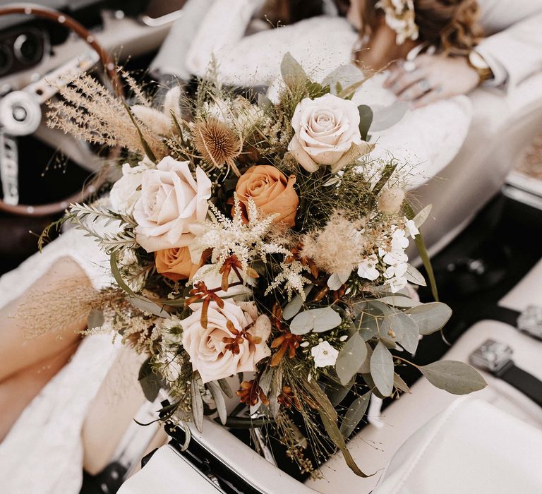 Boho wedding bouquet with cream and orange roses, green foliage and dried grasses 