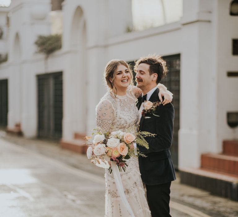 Groom kisses his bride outdoors as she holds floral bouquet on their wedding day