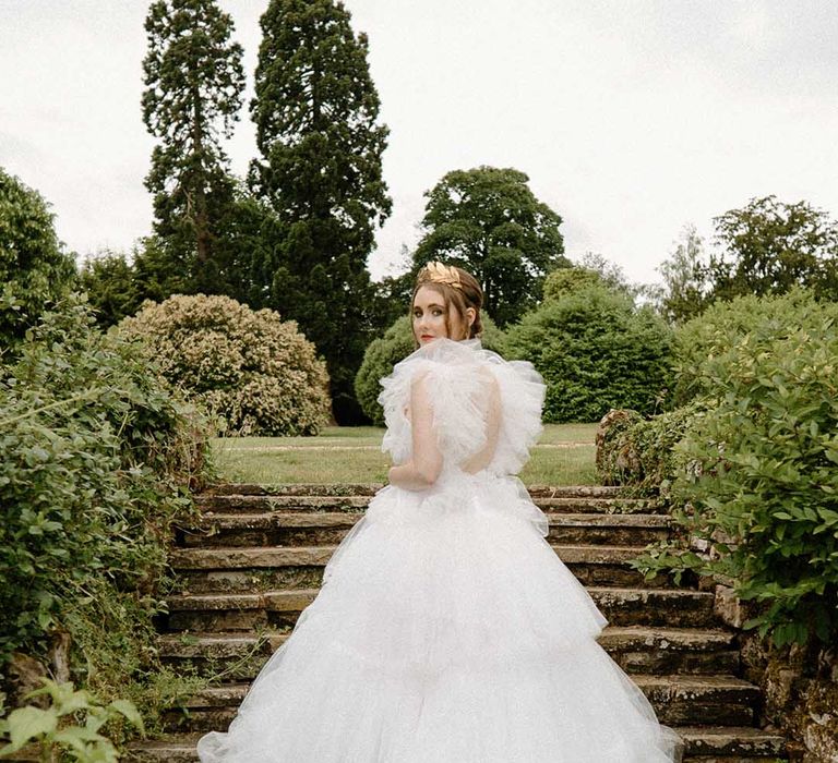 Bride in a tulle wedding dress standing on the steps in the gardens at Bourton Hall wedding venue 