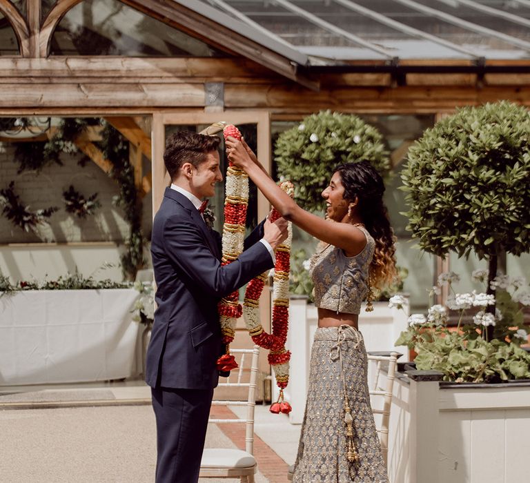 Bride & groom place colourful floral garland around one another's neck on their wedding day | Joshua Gooding Photography