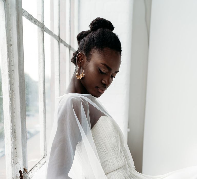 Black bride with afro hair bridal updo and gold earrings in a tulle cape by Rebecca Anne Designs