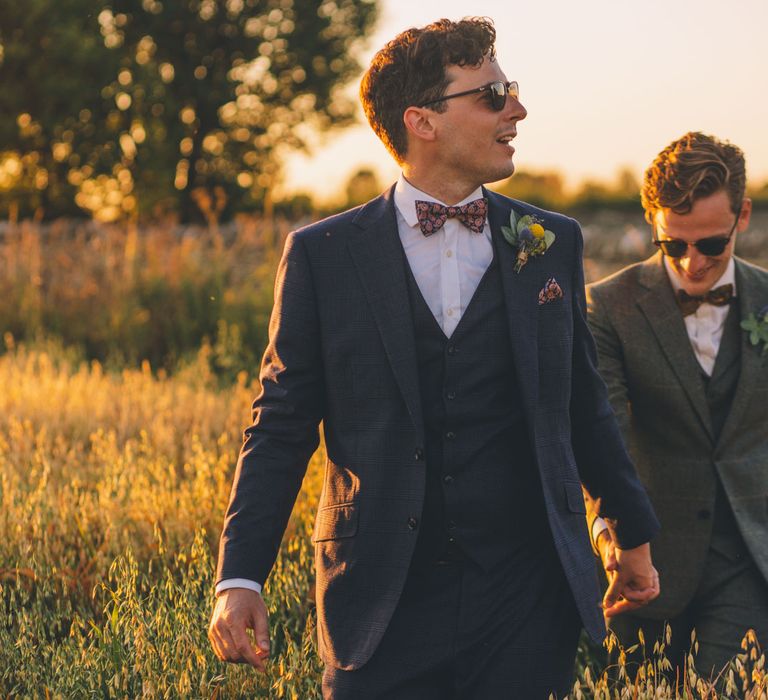 Grooms walk together through golden fields during sunset on their wedding day | Story + Colour