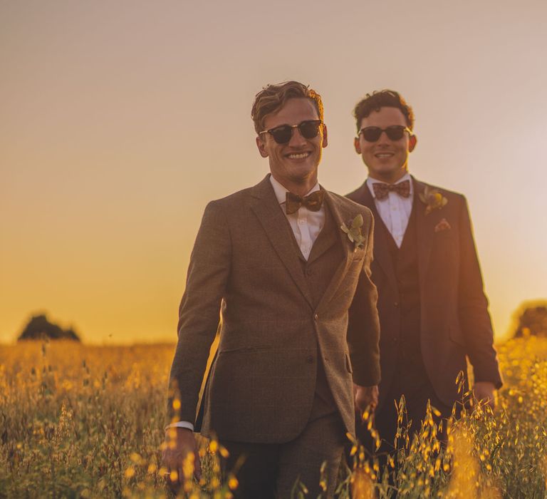 Grooms walk hand in hand together through golden fields as the sun sets behind them | Story + Colour