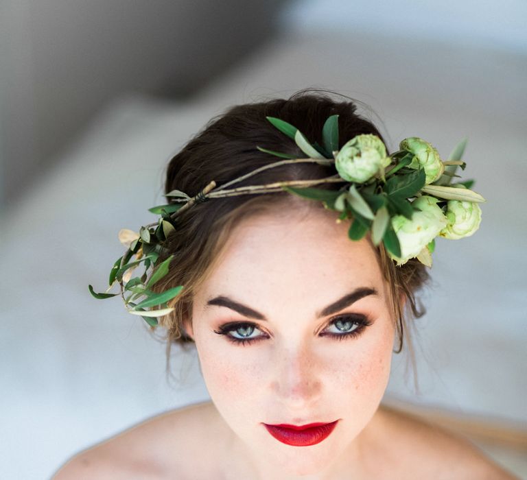 Beautiful wedding makeup with bold red lipstick, smokey eye make up and black eyeliner wearing a green foliage crown 