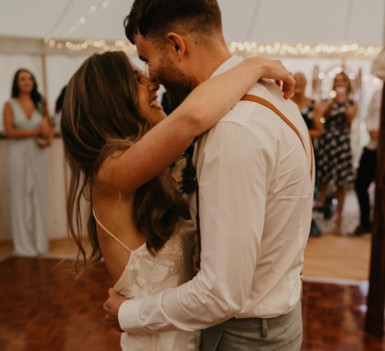 Bride wraps her arms around groom as they dance during marquee reception | Mark Bamforth Photography