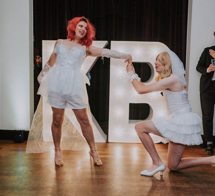 Grooms dance on their wedding day in drag beside personalised light up lettering | Kim Williams Weddings