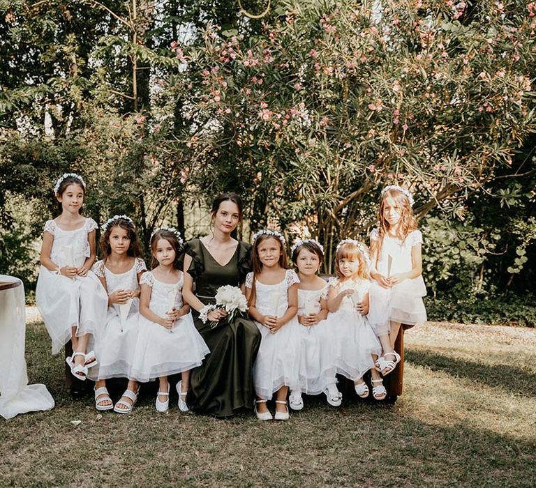 Bridesmaid wearing deep green silk dress sits beside flower girls who wear white floral crowns | Royal Studio