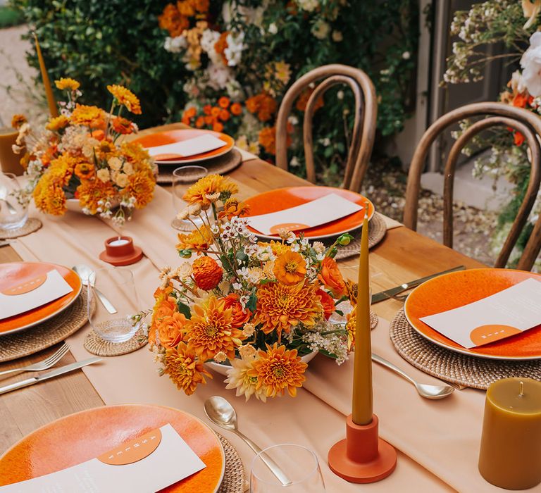 Orange wedding table decor with wicker place mats, coloured tableware, floral centrepiece and taper candles 