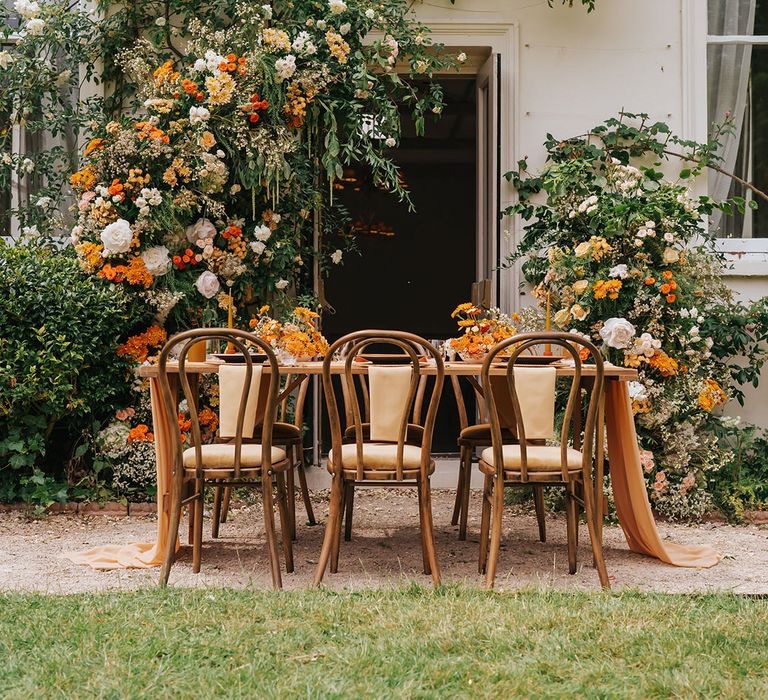 Orange outdoor wedding tablescape with floral arrangement, wooden furniture and table decor 