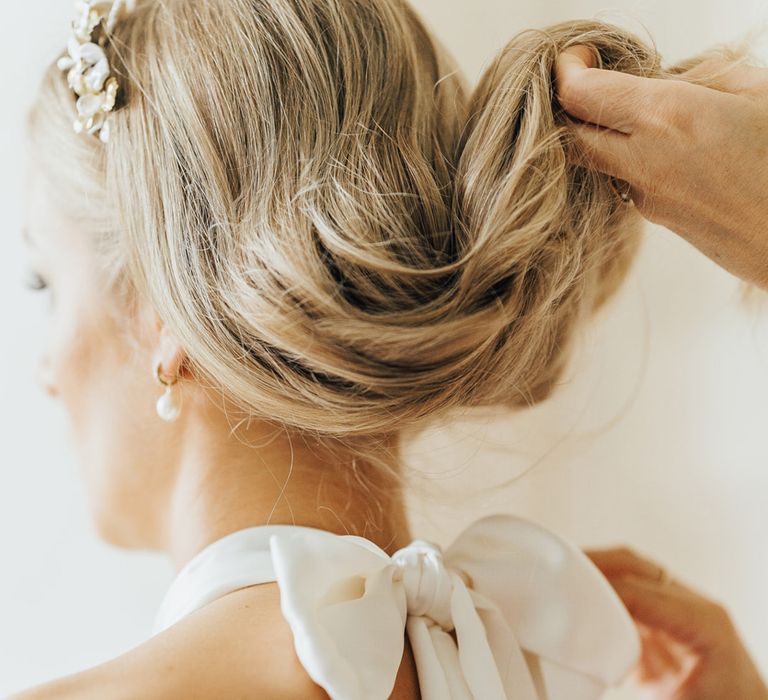 Wedding guest lifts up brides curled hair to reveal bow tied wedding dress