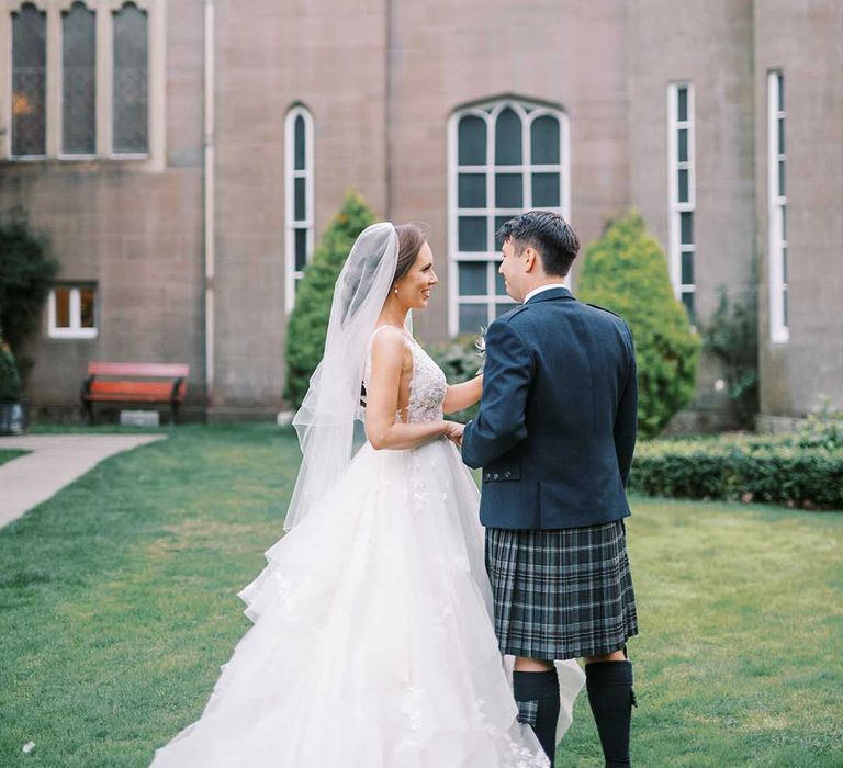 Bride in a layered tulle wedding dress and groom in a blue and green tartan kilt holding hands at Drumtochty castle 