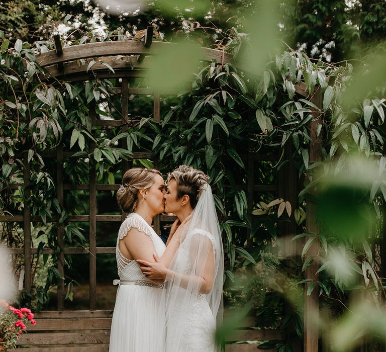 Brides kiss outdoors on their wedding day