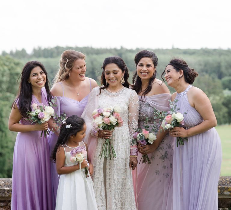 Bride stands with her bridesmaids who wear pastel purple bridesmaid gowns 