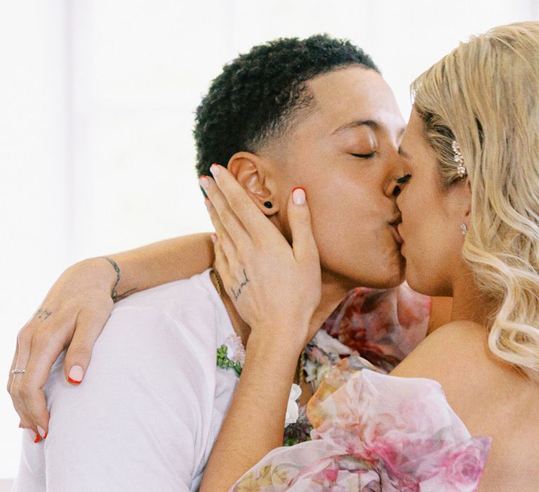 Bride with blonde wavy hair and red manicured nails kissing her partner 