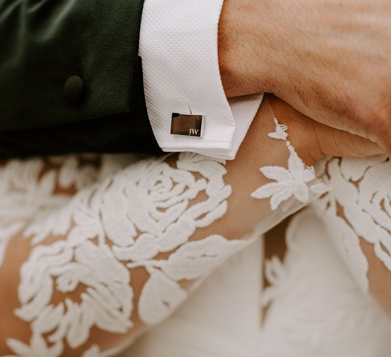 Personalised cufflinks with the groom's initials on as he holds hands with the bride