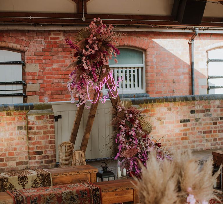 Prestwold Hall Barn wedding styling with wooden benches, wool rugs, lanterns and wooden frame altar decorated with a pink neon sign and flowers