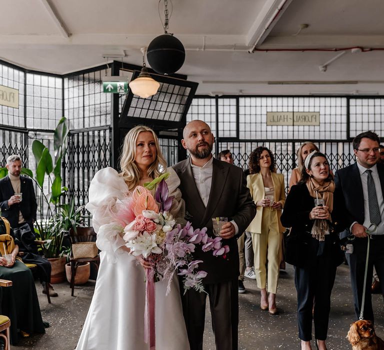 Emotional bride in a princess wedding dress with sheer sleeves holding a lilac orchid bouquet at her drinks reception at Floral Hall