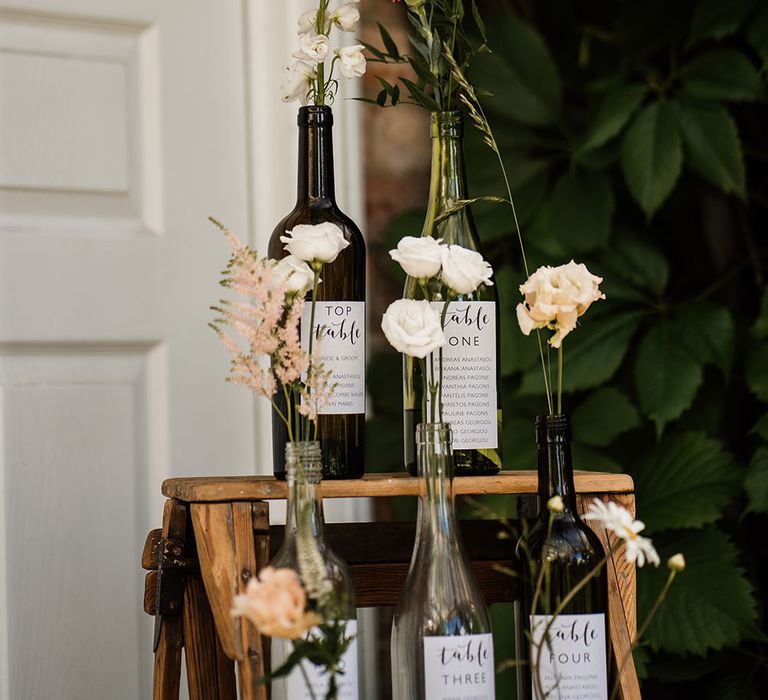 Wooden ladder complete with DIY wine bottles finished with small floral displays and white labels with table numbers 