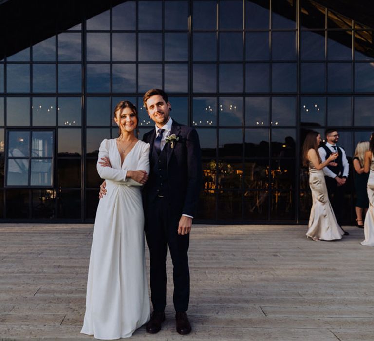 Bride and groom stand with their arms around each other in front of the incredible windows at The Barn at Botley Hill wedding venue 