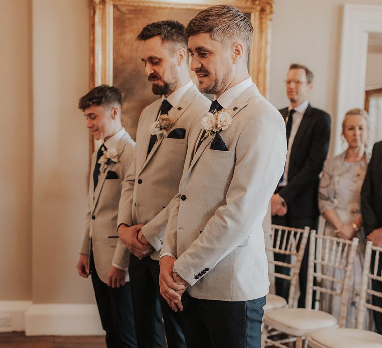 Groom stands with groomsmen in matching grey suit jackets, blue ties and handkerchiefs and black trousers for the wedding 