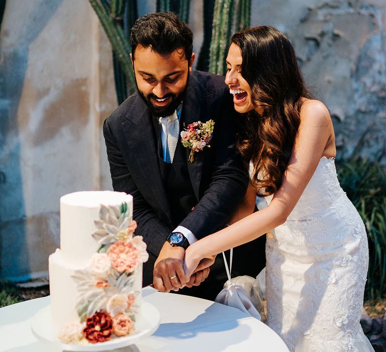 Bride & groom cut two-tier wedding cake with white frosting and colourful frosted florals 