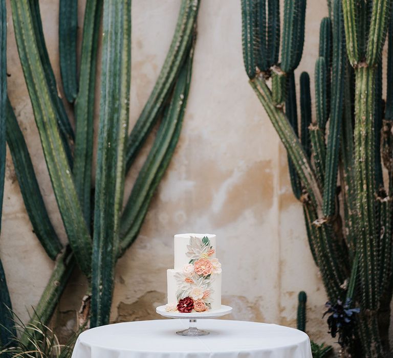 Two-tier white frosted wedding cake complete with brightly frosted floral decor to one side