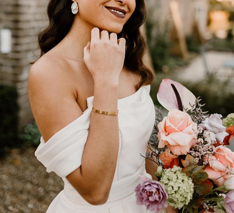 Bride with dark lipstick and gold eyeshadow in an off the shoulder wedding dress holding a pretty wedding bouquet 