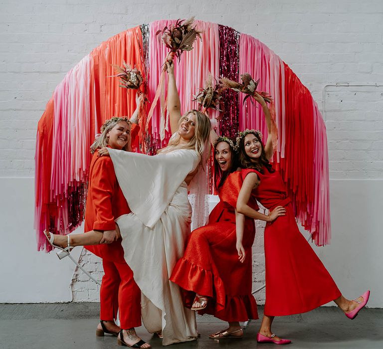 Bride and bridesmaids stand in front of bright pink, red and silver DIY wedding streamer decor 