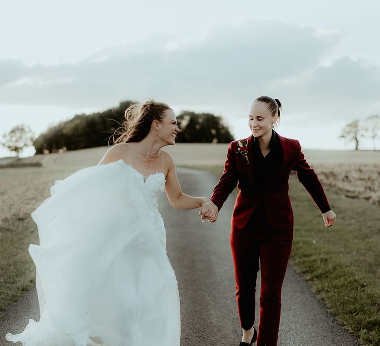 Bride in off the shoulder flower wedding dress smiling with the bride in a burgundy suit 