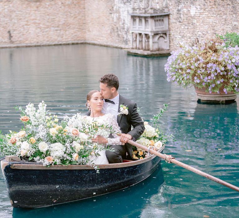 The groom in black tie rows himself and the bride on their wedding day surrounded by yellow wedding flowers 