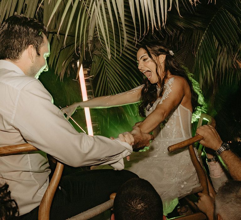 Bride & groom are lifted in the air on seats during wedding reception outdoors