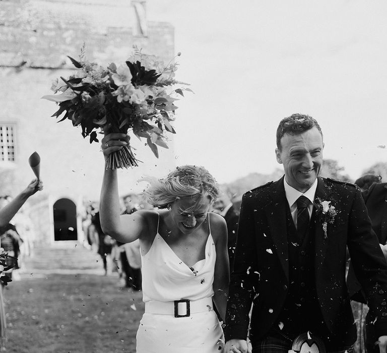 Bride & groom walk through confetti in black & white image 