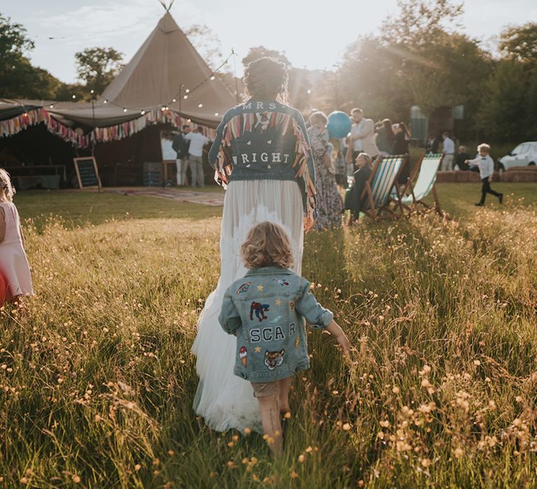 Bride walks with her son in personalised denim jackets during golden hour 