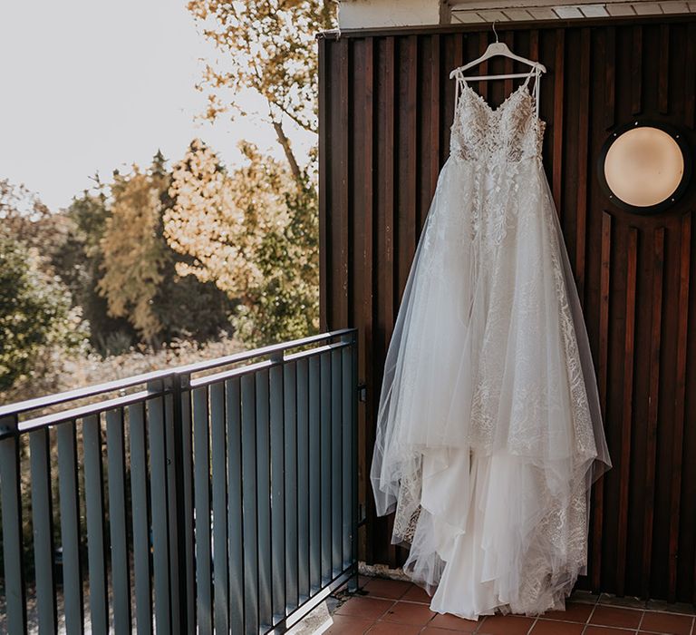 The bride's lace wedding dress is hanging on white wooden hanger with tulle skirt 