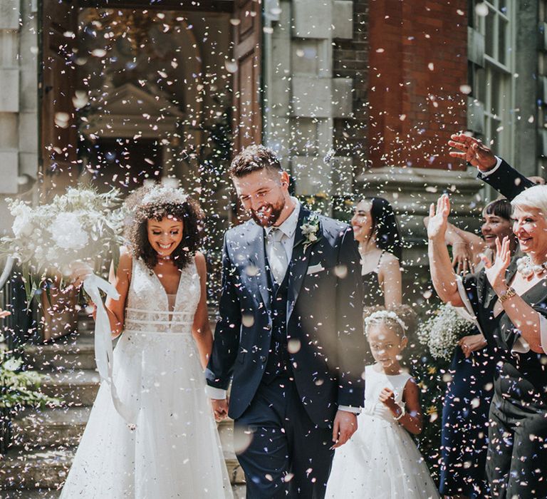 Bride in lace wedding dress with boho styled skirt walks through white confetti with her groom