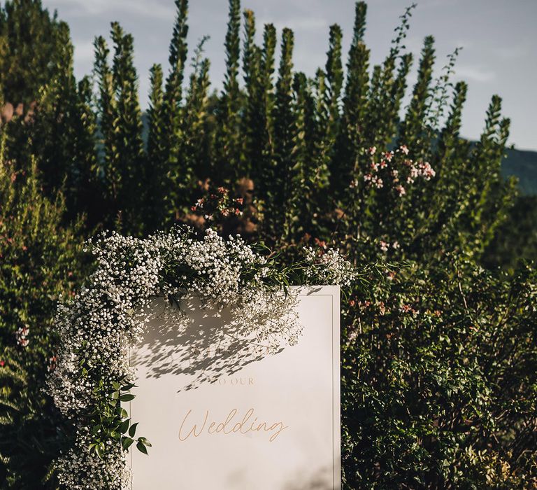 White classic wedding signage with gold writing surrounded by babys breath floral decor