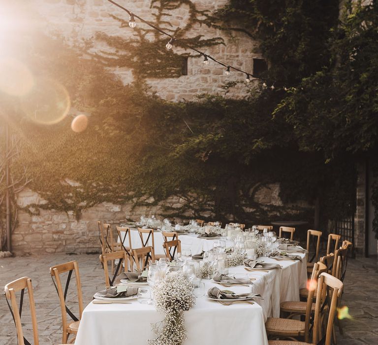 Golden hour sun shines across winding reception tables complete with babys breath table runner and green colour scheme 