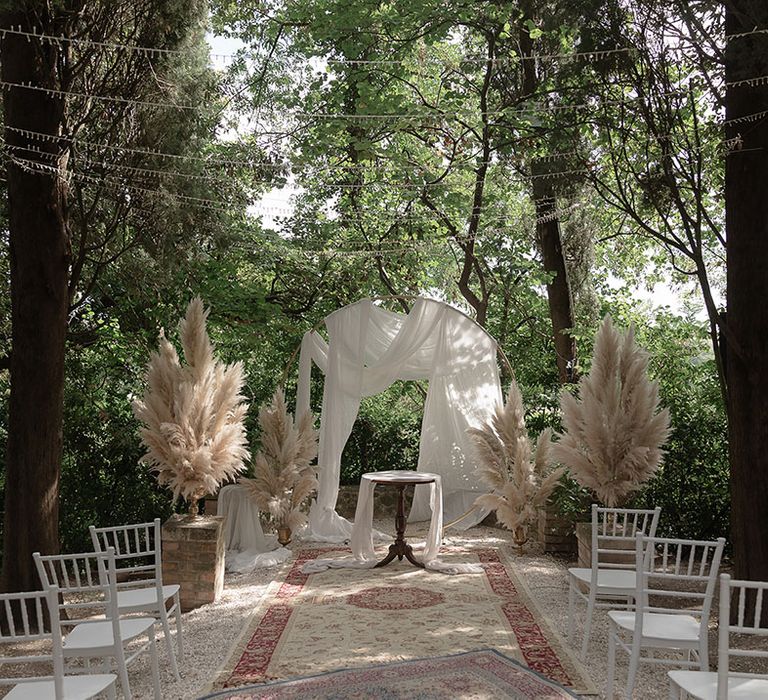 Moroccan styled rugs line aisle outdoors complete with draped archway and pampas grass decor 