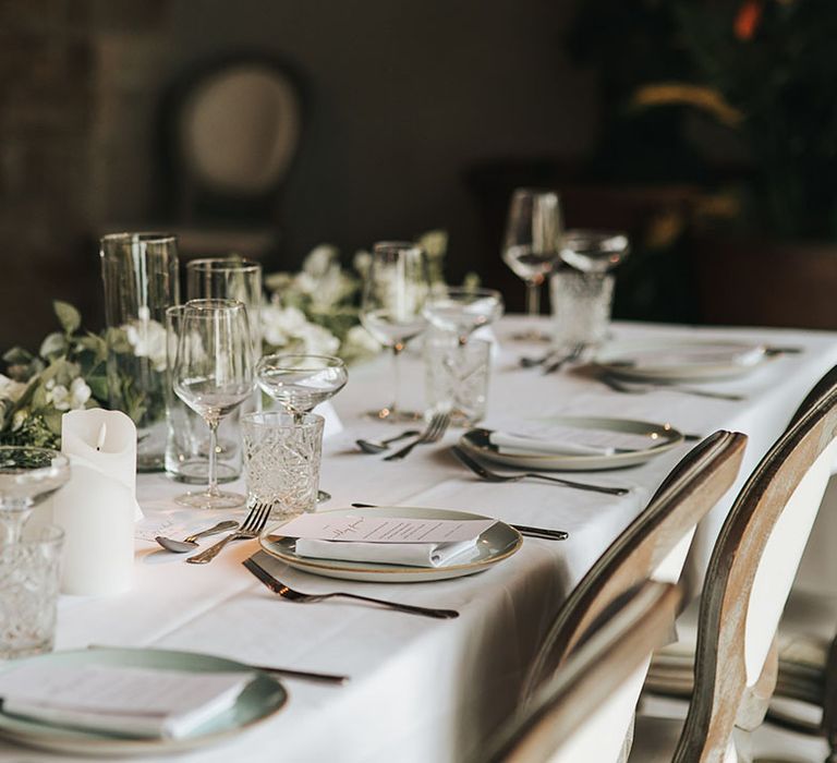 Simple and minimal traditional wedding tablescape with white pillar candles, table cloths and place names on speckled plates 