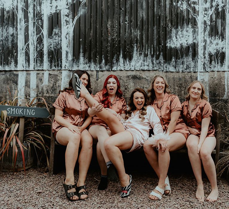 Bridesmaids in burnt orange satin pyjamas with the bride in pink satin pyjamas with pink feather cuffs 