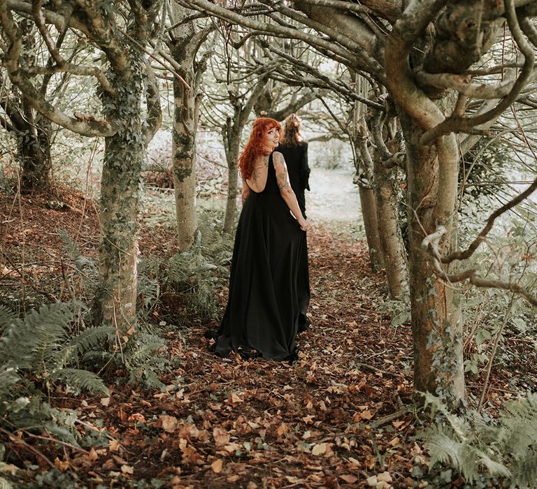 Bride in open back detail black wedding dress walking through the woods at Westcott Barton Devon wedding venue 