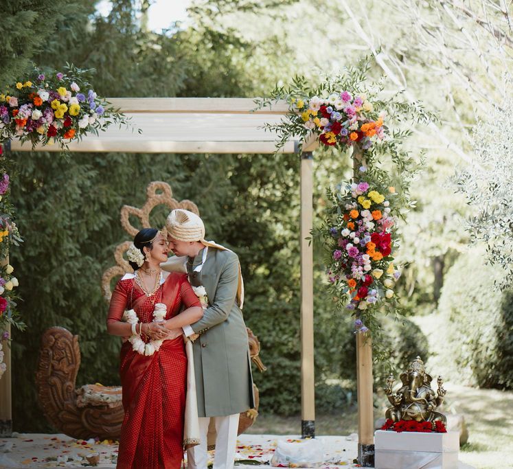 Bride in a red lehenga and groom in a green Sherwani kissing at their Hindu wedding in Provence 