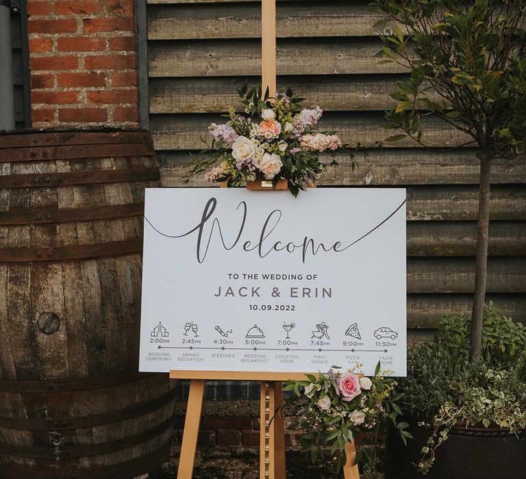 Black and white wedding welcome and order of the day sign on a wooden easel with pastel flowers for Dove Barn Weddings 