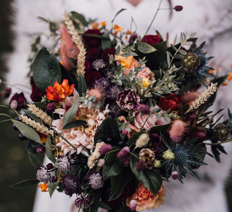 Purple, pink, yellow, and orange bridal bouquet with foliage, thistles, and pink bunny grass 