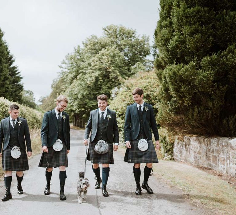 Groomsmen and groom wearing matching dark grey blazers and waistcoats, dark tartan ties with white flower boutonnieres, dark grey and blue tartan kilts and wedding sporrans 