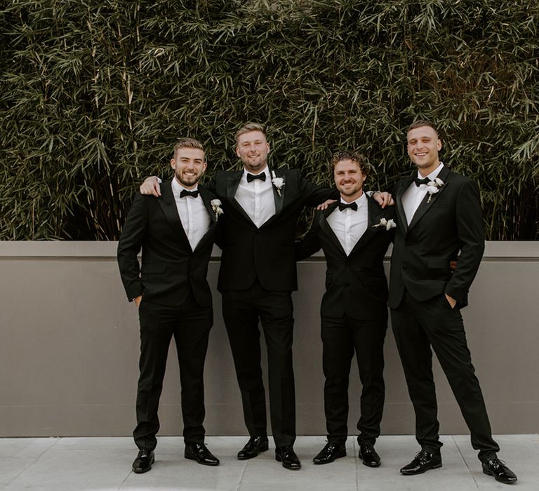 Groom and groomsmen all wearing matching black tuxedos and white flower buttonholes for modern minimal style city wedding 