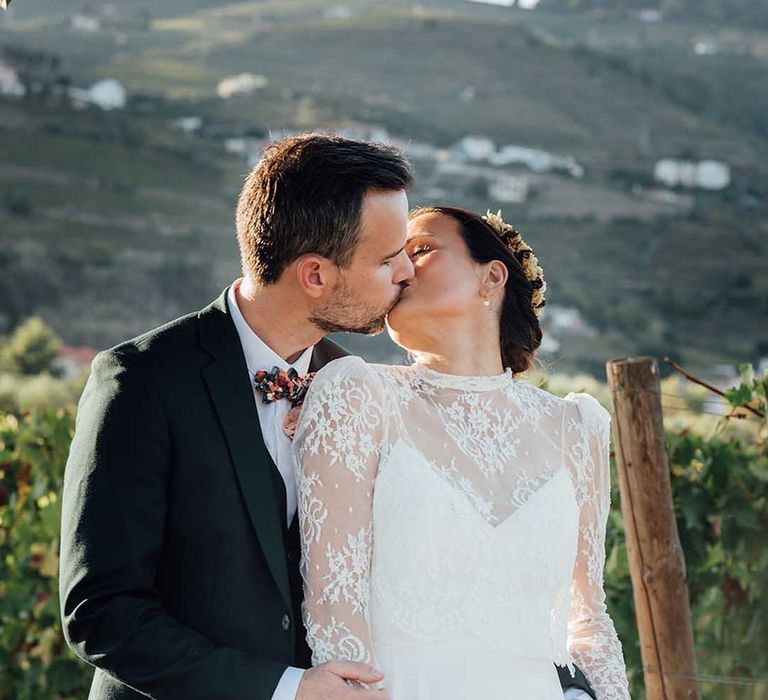 groom in black suit kissing his boho bride in a lace wedding dress with long sleeves 