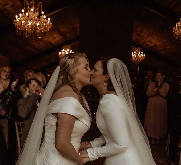 Bride in long sleeve deep v wedding dress and church length veil kissing bride in satin short sleeve deep v wedding dress and church length veil at the alter of Hidden River Cabins 